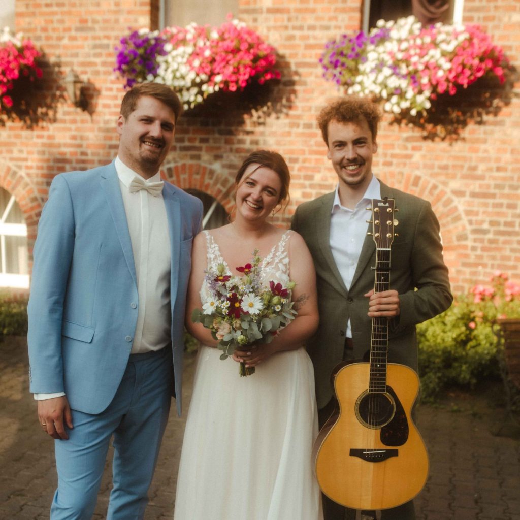 Hochzeitssänger Köln mit Gitarre beim musikalischen Sektempfang mit dem Brautpaar im Außenbereich von Hof Bleckmann, NRW.
